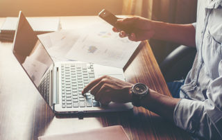 Businessman hands using cell phone with laptop at office desk.