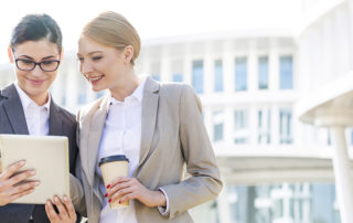 Happy businesswomen using digital tablet outside office building